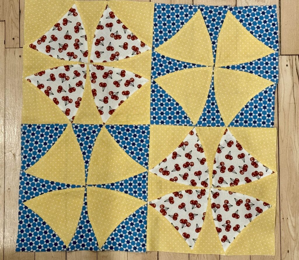 Winding Ways four-block quilt made with white fabric with cherry designs, yellow fabric with white polka dots, and blue fabric with star designs.