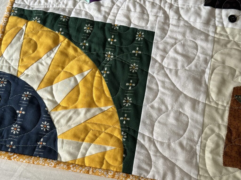 New York Beauty quilt block in green, blue, gold, and white fabrics quilted with a double-heart motif.